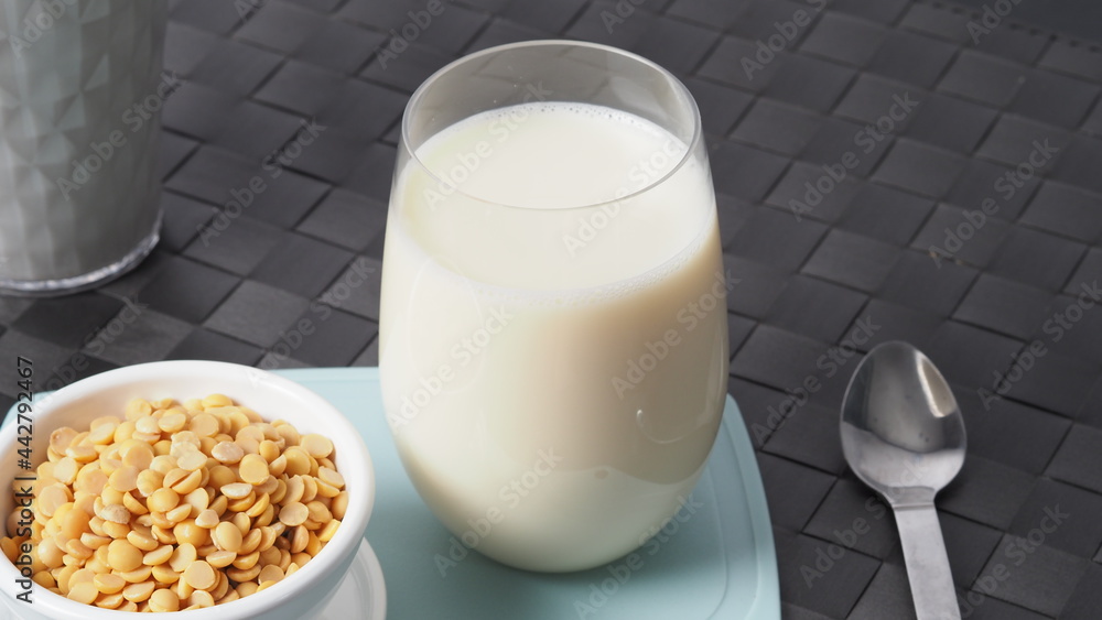 Soy milk with no sugar added in a glass on a green color plastic plate mat. Close-up images of home made healthy soy milk drink and soy beans in small bowl. Black background in a studio shot. Soymilk. Soy milk with no sugar added in a glass on a green color plastic plate mat. Close-up images of home made healthy soy milk drink and soy beans in small bowl. Black background in a studio shot. Soymilk.