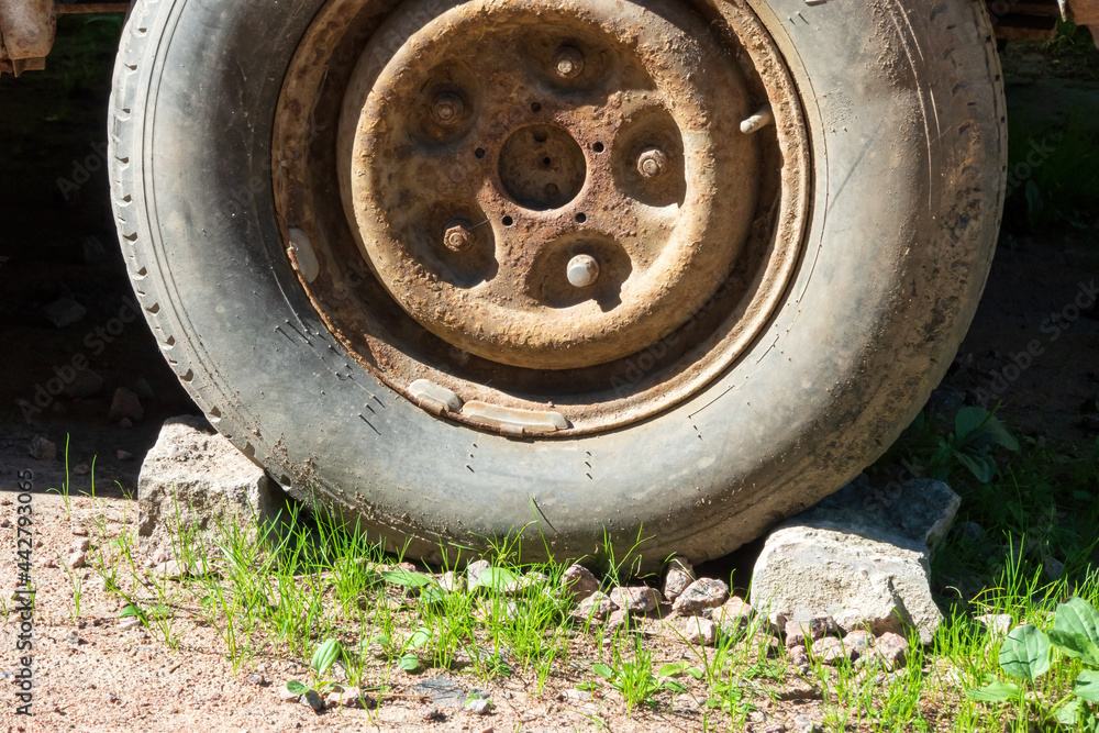 An old car wheel is fixed on both sides with gray mud stones. There is a rusted disc with screws and a worn tire. Background. Texture.