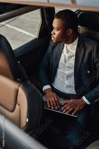 Serious black employee working on laptop inside of car