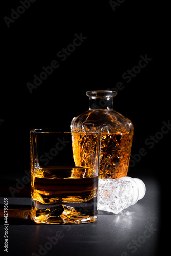 Close-up of a crystal glass along with a bottle full of whiskey on black background.