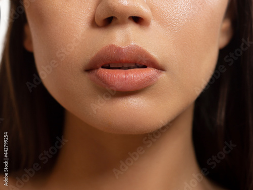 Close-up of woman's lips with fashion natural beige lipstick makeup. Macro sexy pale lipgloss make-up . Gentle pure skin and wavy brunet hair. Cosmetology, Spa, increase in lips photo