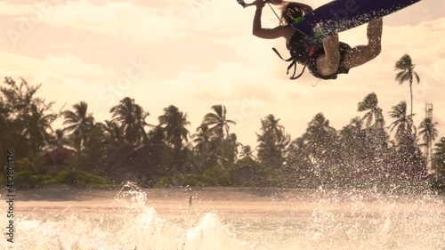SLOW MOTION, CLOSE UP: Extreme female kitesurfer riding in Zanzibar jumps and does a superman trick on a sunny summer evening. Spectacular shot of a kiteboarder doing a trick in the air while surfing.