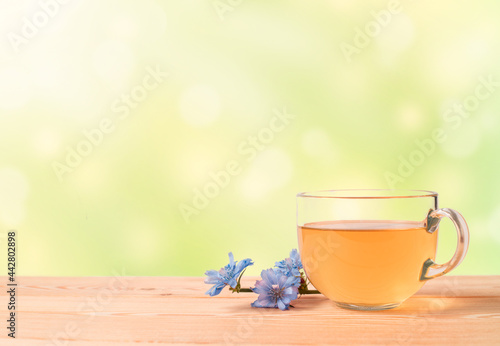 a cup of herbal tea and blue flowers on a wooden table on a green blurred background