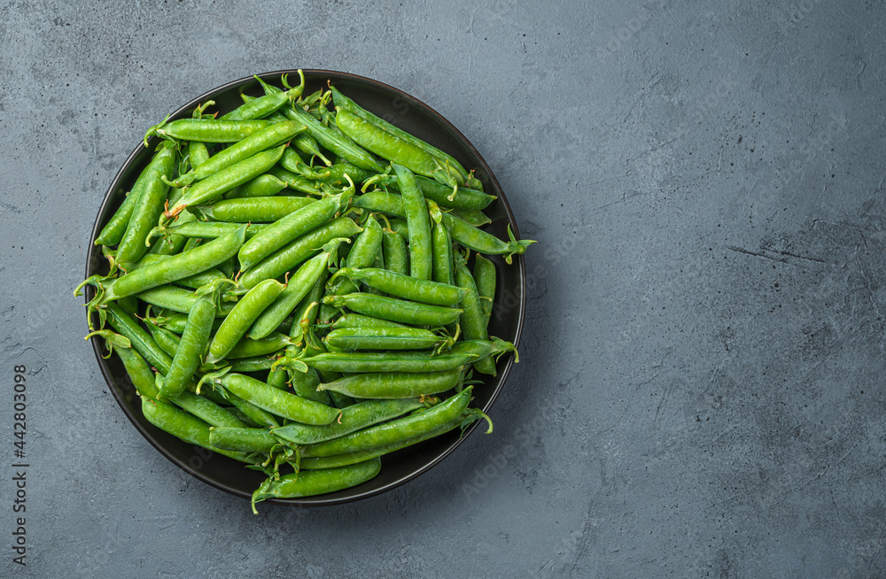 A plate with pea pods on a gray background. Copy space.