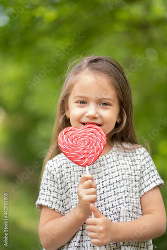 Little girl licking big heart-shaped lollipop