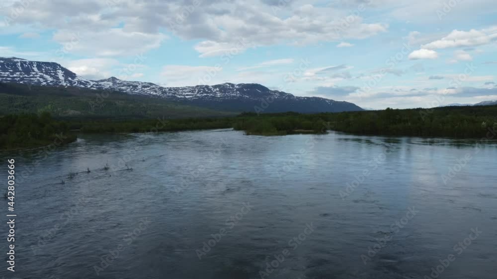 massive river flood moving fast during the yearly spring time melting period with lush green forest and blue sky with snow patched mountain backdrop, aerial hot massive river flood moving fast during the yearly spring time melting period with lush green forest and blue sky with snow patched mountain backdrop, aerial hot