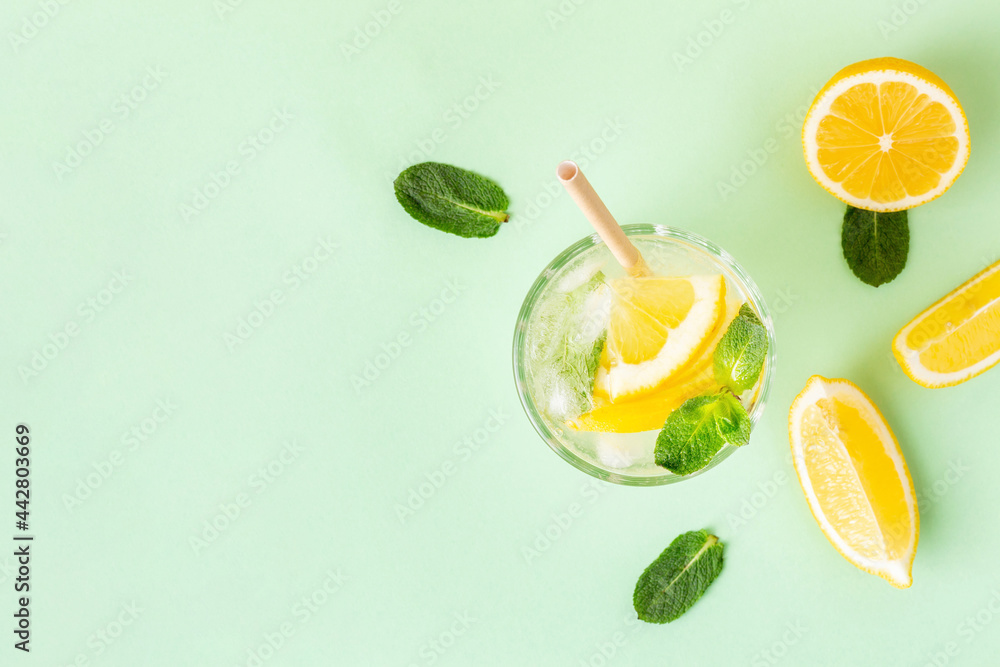 Ice lemon water or lemonade with mint on a green background. A glass of fresh fruit drink for summer heat. - obrazy, fototapety, plakaty 