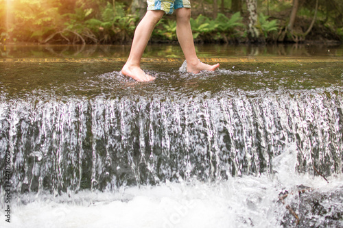 Kids legs walkingin watere  in stream in the summer. Outdoor, barefoot, holiday concept