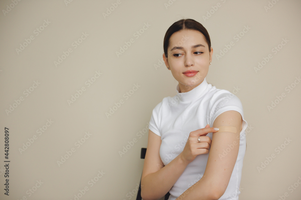 Brunette woman is smiling after getting the vaccine on her hand posing on a white studio wall Brunette woman is smiling after getting the vaccine on her hand posing on a white studio wall