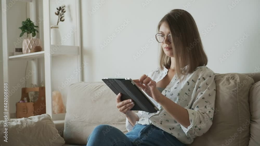 woman in eyeglasses using digital tablet sitting on sofa at home woman in eyeglasses using digital tablet sitting on sofa at home