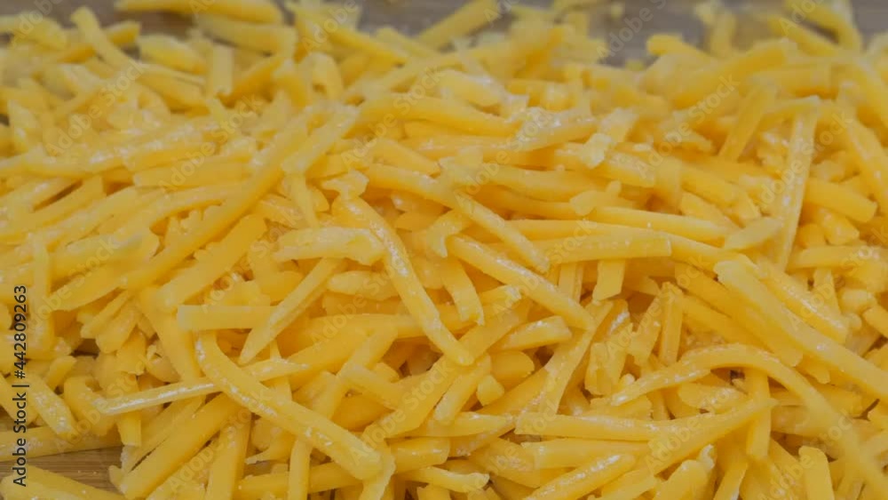 Grated cheddar cheese falling into a mound on a cutting board Grated cheddar cheese falling into a mound on a cutting board