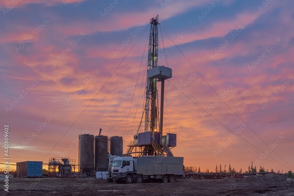 Drilling of deep well at the oil and gas field. In the foreground, cementing unit and cement bins. Compound cementing well. Beautiful northern sunset