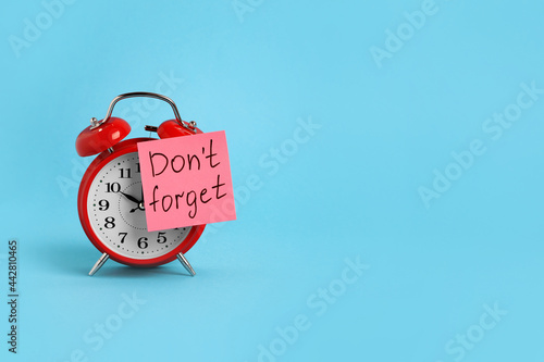 Alarm clock and reminder note with phrase Don't forget on light blue background, space for text © New Africa