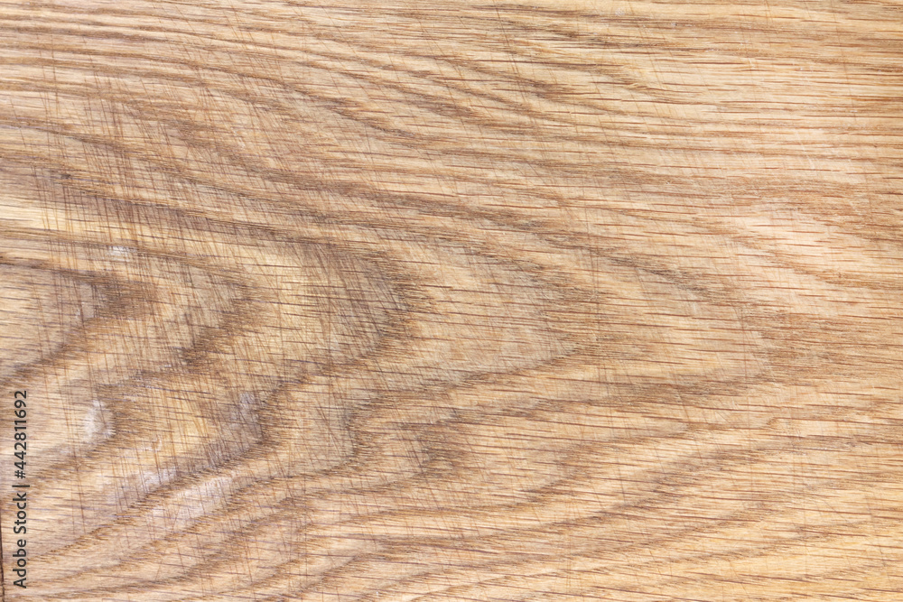 An oak kitchen chopping board covered in knife scratches. Uneven texture of a polished board with a pattern and streaks of natural wood. An oak kitchen chopping board covered in knife scratches. Uneven texture of a polished board with a pattern and streaks of natural wood.