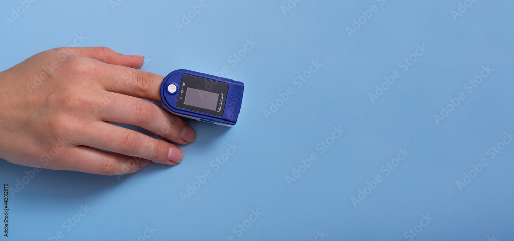 A pulse oximeter is on the woman's hand. A pulse oximeter used to measure heart rate and oxygen levels.. Covid-19. Banner A pulse oximeter is on the woman's hand. A pulse oximeter used to measure heart rate and oxygen levels.. Covid-19. Banner