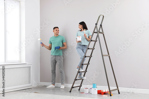 Young couple painting wall with roller and brush indoors