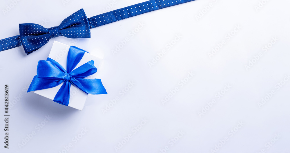 Fathers gift. White box with bow ribbon, blue bowtie or tie on light background. Concept of Fathers Day greeting card, copy space for text.
