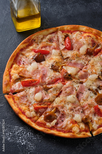 Pizza with tomatoes, bacon, pickled onions, honey mushrooms, mozzarella cheese, spices and tomato sauce. On a dark background.