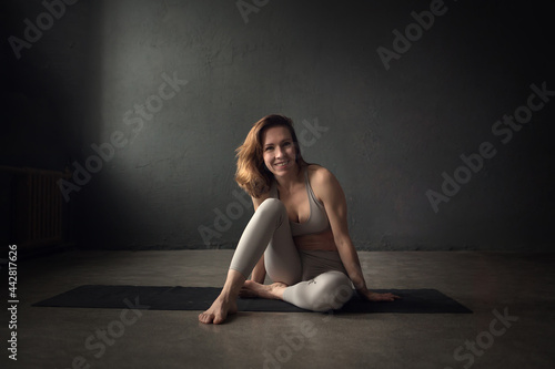 A slim beautifully lighted young woman is doing yoga in a dark room. Image with selective focus and toning