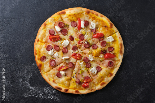 Pizza with tomatoes, ham, onions, feta cheese, mozzarella cheese, spicy sausages, spices and mustard sauce. Flat lay. On a dark background.