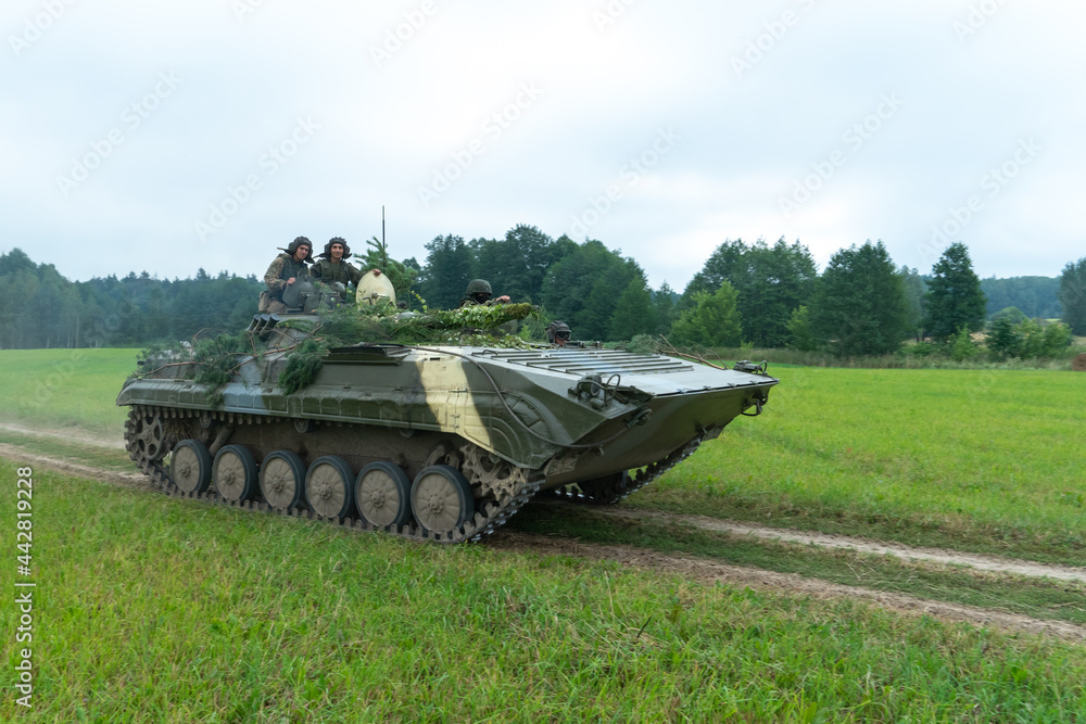 infantry combat vehicle rides on a dirt road along a field against the background of a forest with soldiers on board. Various military equipment at the exercises infantry combat vehicle rides on a dirt road along a field against the background of a forest with soldiers on board. Various military equipment at the exercises