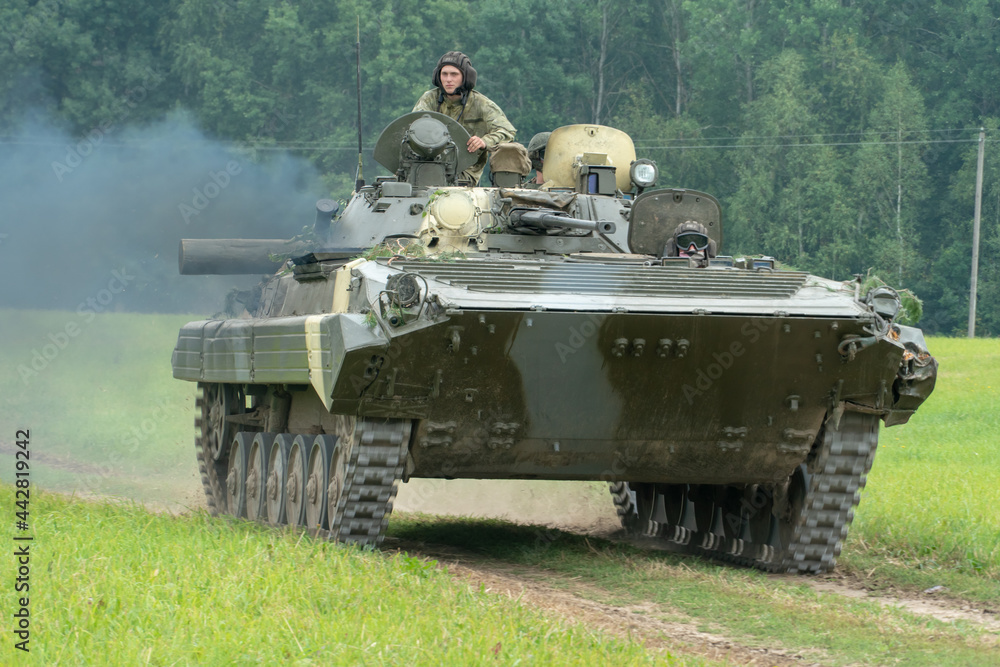 infantry combat vehicle rides on a dirt road along a field against the background of a forest with soldiers on board. Various military equipment at the exercises