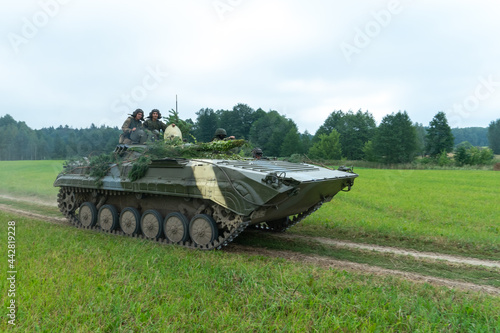 infantry combat vehicle rides on a dirt road along a field against the background of a forest with soldiers on board. Various military equipment at the exercises