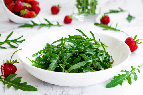 Summer salad of strawberry with arugula, spinach leaves in white plate on marble table with salad leaves and fresh strawberry fruits around. Strawberry salad recipe DIY. Step 1.