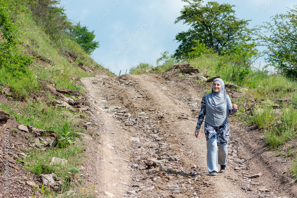 Young muslim girl wearing sport clothes walking alone on the rural mountain road. Woman with hijab in the nature. Islam religion concept Young muslim girl wearing sport clothes walking alone on the rural mountain road. Woman with hijab in the nature. Islam religion concept