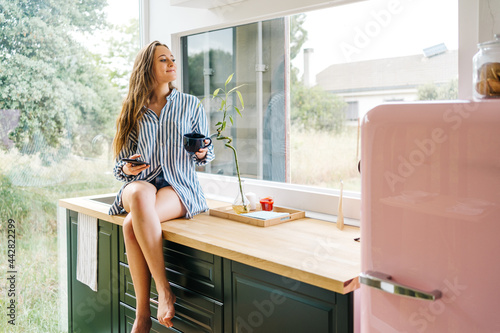 side view  of young millennial using her mobile phone in her kitchen