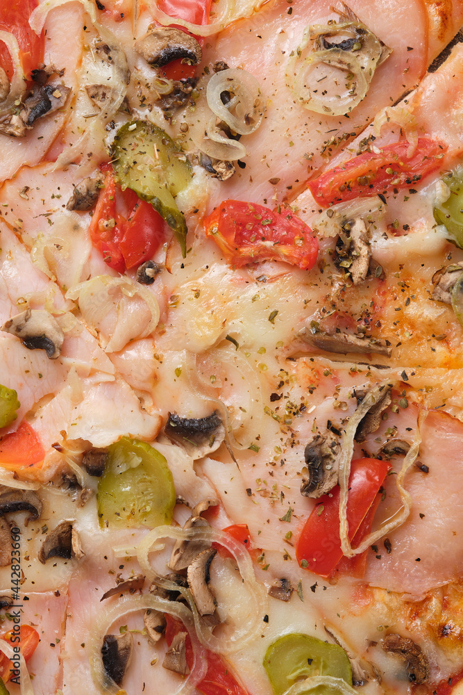 Pizza with tomatoes, cucumber, ham, mushrooms, onions, cheese and spices. A closeup of a pizza.