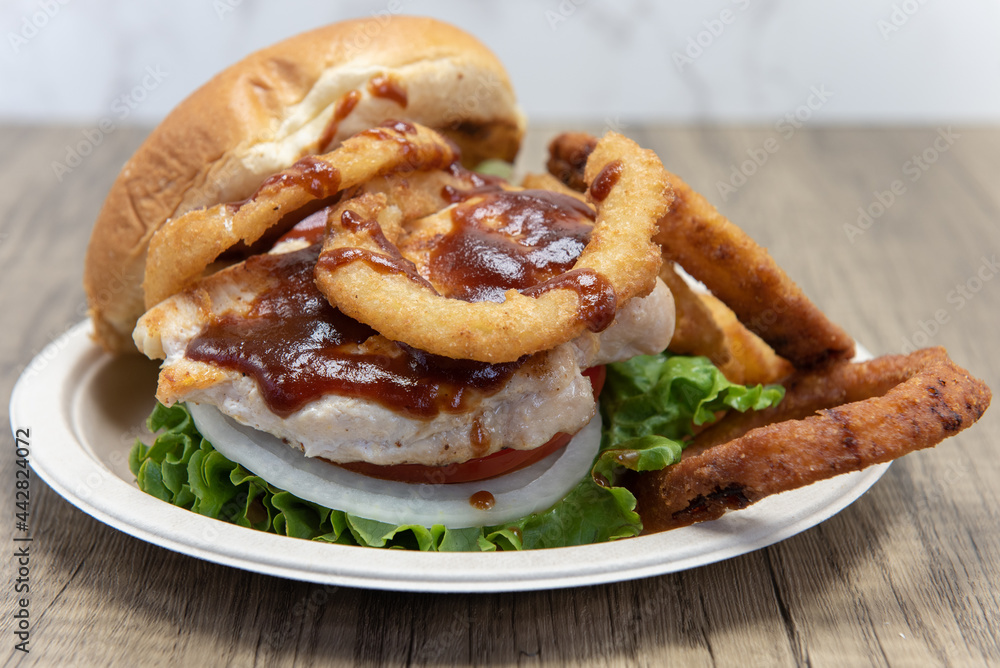 Barbeque chicken sandwich stacked tall in the toasted bun with huge onion rings on the side to fill the entire plate Barbeque chicken sandwich stacked tall in the toasted bun with huge onion rings on the side to fill the entire plate