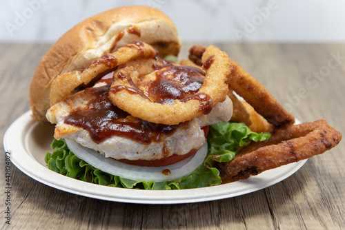 Barbeque chicken sandwich stacked tall in the toasted bun with huge onion rings on the side to fill the entire plate