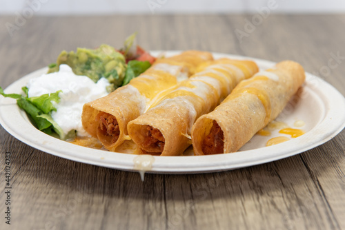 Three crispy deep fried chicken taquitos covered with melted cheese and served with a scoop of sour cream, guacamole, and pico de gallo photo
