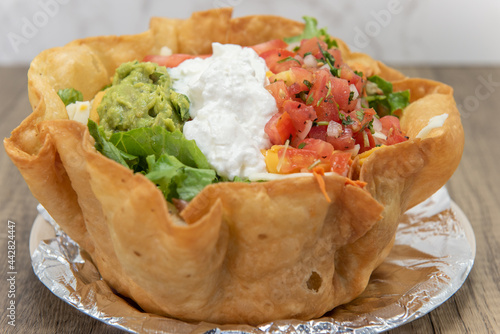 Huge tostada crispy bowl filled completely and topped with scoops of sour cream, guacamole, and pico de gallo photo