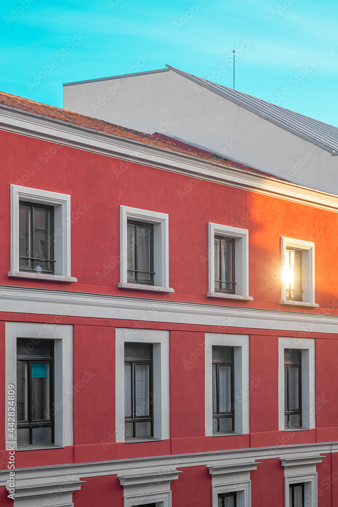 red facade of a building in the center of Madrid at sunset, with a ray of sunlight reflecting in a window