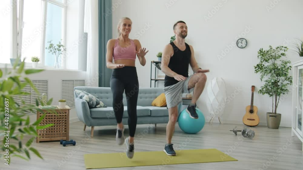 Slow motion of girl and guy in sportswear jumping doing sports indoors at home enjoying active exercise smiling. Modern people and workout concept. Slow motion of girl and guy in sportswear jumping doing sports indoors at home enjoying active exercise smiling. Modern people and workout concept.