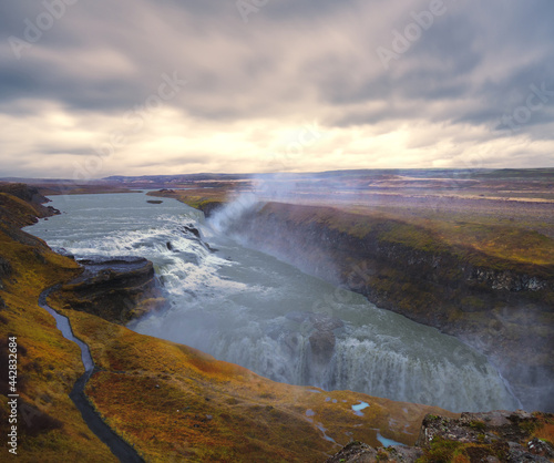 The Gullfoss waterfall in Iceland shimmers in the evening sunset under a cloudy sky.