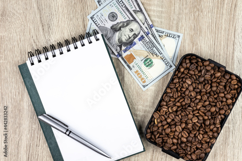 Top view mockup of open blank notebook on spiral, automatic pen. 100 dollar banknotes and samples rosted coffee beans, conceptualizing agricultural commodities. on a wooden table photo