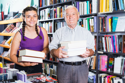 Grandpa with granddaughter are demonstrating their purchases in bookstore.