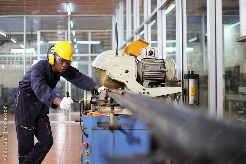 African American mechanic engineer worker wearing safety equipment is cutting copper tube using sawing machine in the factory African American mechanic engineer worker wearing safety equipment is cutting copper tube using sawing machine in the factory