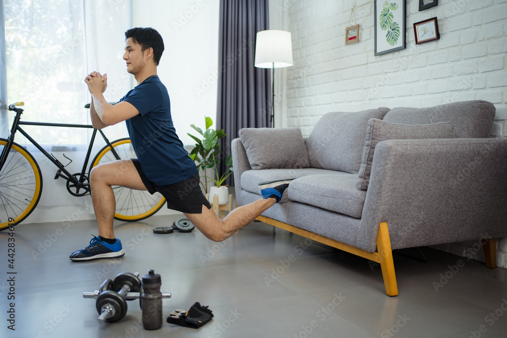 Fototapeta premium Active young man watching online training video on laptop. He's stretching during his morning workout at home.