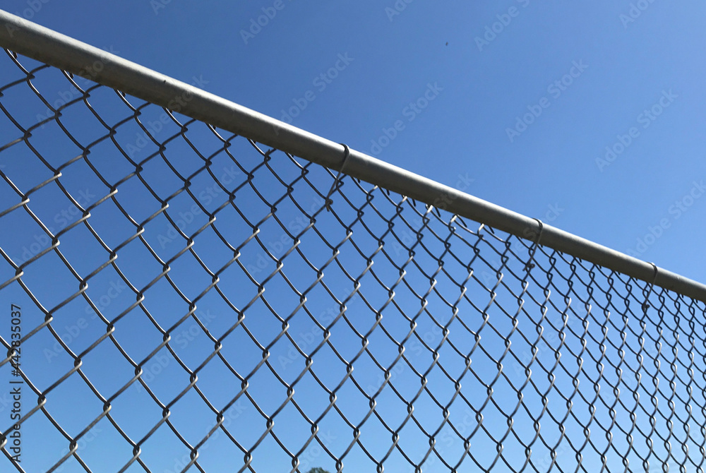 Closeup of a metal chain link fence with a clear blue sky background Closeup of a metal chain link fence with a clear blue sky background