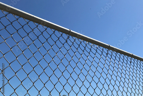 Closeup of a metal chain link fence with a clear blue sky background © JudithAnne