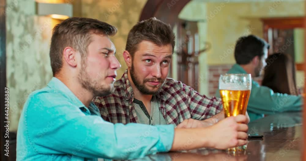 Smiling carefree friends enjoying drinking together in bar. Group of happy young men drinking cold draft beer, chatting and having good time at pub. Laughing men on night out drinking beer on counter. Smiling carefree friends enjoying drinking together in bar. Group of happy young men drinking cold draft beer, chatting and having good time at pub. Laughing men on night out drinking beer on counter.