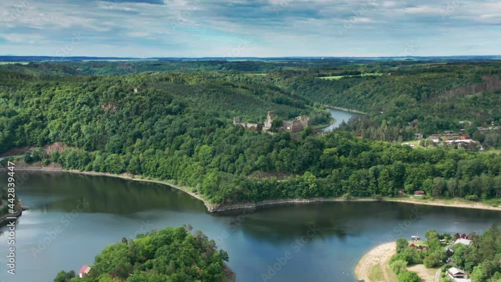 A picturesque panorama opens up on a flight approaching a Cornstejn castle: overcoming a river loop spectator sees a derelict stone fortress rising on an overgrown hill. A green valley extends beyond. A picturesque panorama opens up on a flight approaching a Cornstejn castle: overcoming a river loop spectator sees a derelict stone fortress rising on an overgrown hill. A green valley extends beyond.