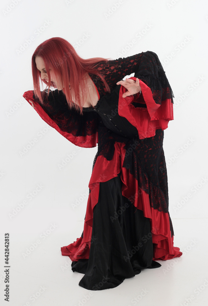 full length portrait of red haired woman wearing long black gothic vampire gown. standing pose on white studio background full length portrait of red haired woman wearing long black gothic vampire gown. standing pose on white studio background