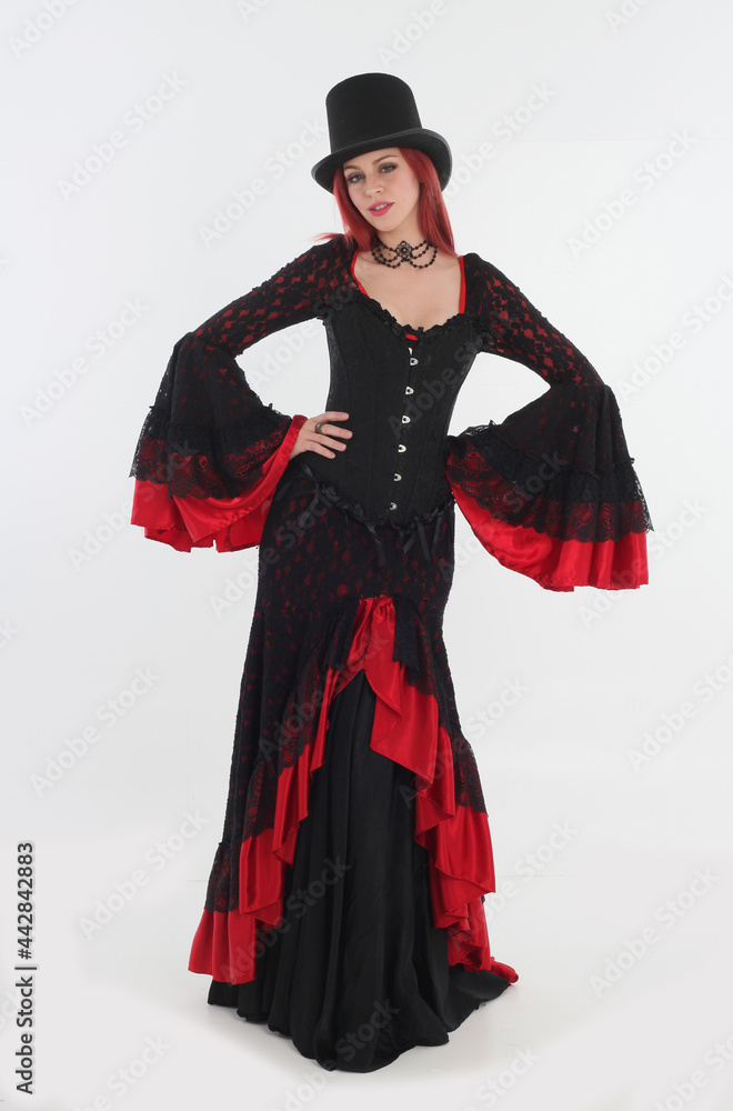 full length portrait of red haired woman wearing long black gothic vampire gown. standing pose on white studio background