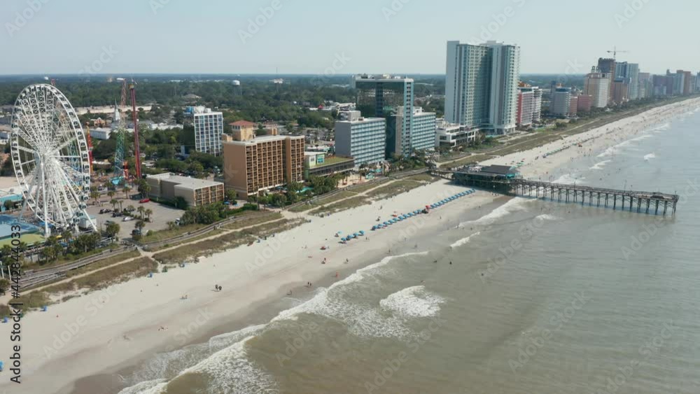 Descending aerial of ocean beach shore coastline. Amusement park and pier with highrise apartments and hotels. Summer vacation fun season. Descending aerial of ocean beach shore coastline. Amusement park and pier with highrise apartments and hotels. Summer vacation fun season.