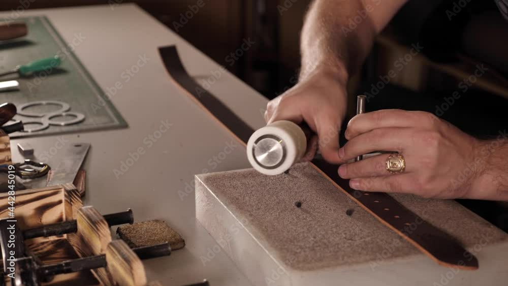 Close up shot of a handmade specialist working with leather, male hands of a craftsman making holes in a leather belt in a small workshop. Slow motion in 4K Close up shot of a handmade specialist working with leather, male hands of a craftsman making holes in a leather belt in a small workshop. Slow motion in 4K
